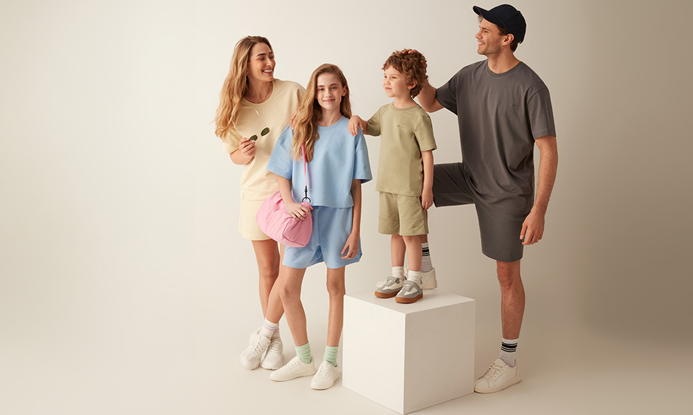 Μια οικογένεια με παστέλ ρούχα ποζάρει μαζί σε ανοιχτόχρωμο φόντο.